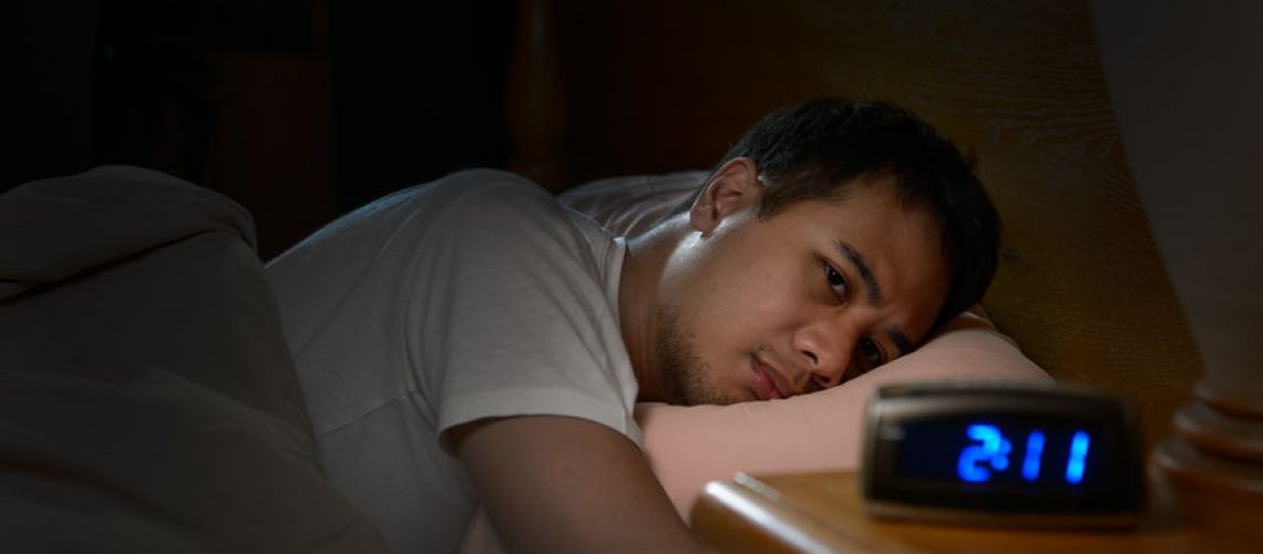 Depressed man suffering from insomnia lying in bed