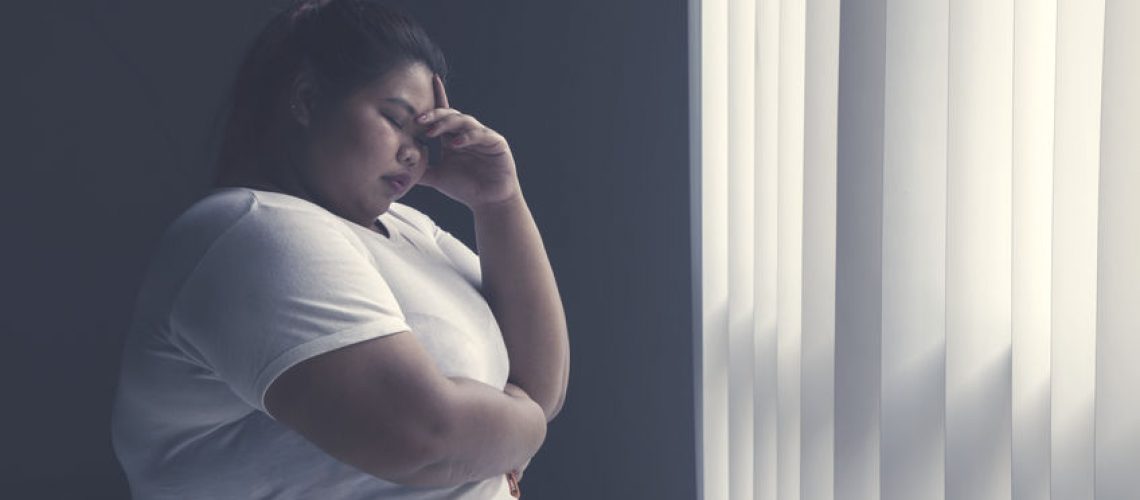 Picture of stressed fat woman having headache while standing by the window